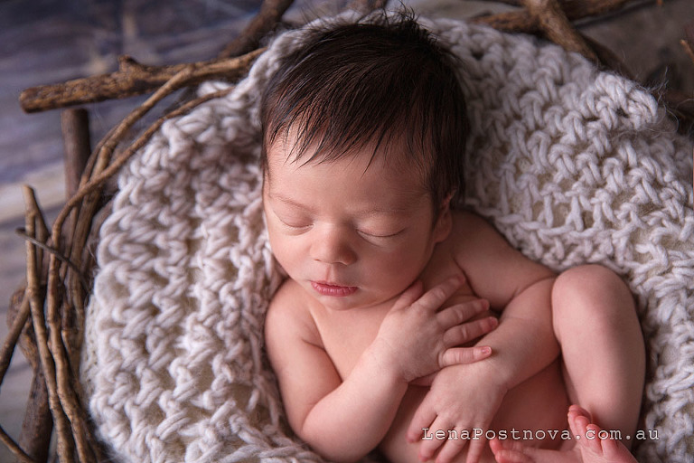 newborn baby boy with the cute long hair sleeping in the prop nest