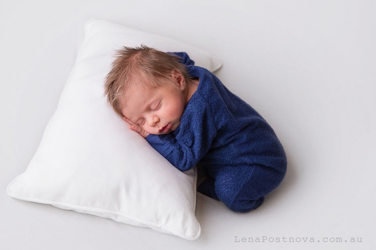 Newborn baby boy sleeping on the pillow wearing blue romper