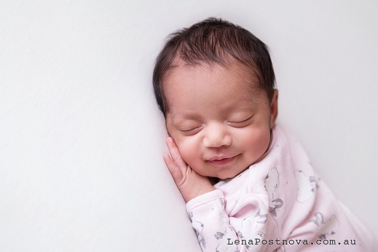 Newborn baby wering pink babysuit sleeping and smiling 