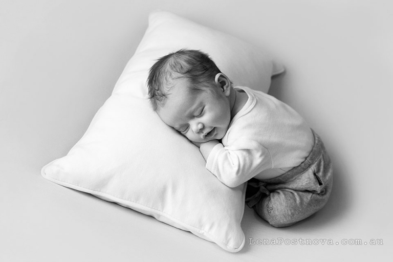 Newborn Photo - Smiling neworn baby wearing white top and grey borrom sleeping on the pillow on the tummy