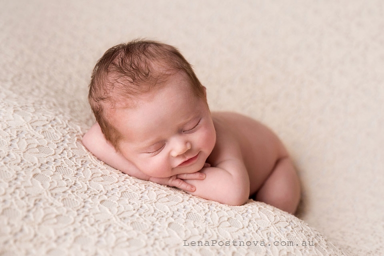 cute newborn baby posed on the tummy hands under the chin and smiling