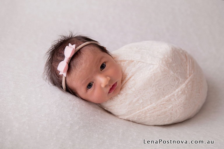 long haired newborn baby swaddled in the cream lace wrap looking at the camera 