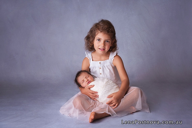 toddler with newborn baby sister in her arms