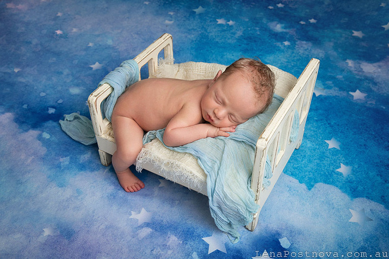 blond curly haired newborn posed at tiny bed on the backdrop with the stars.