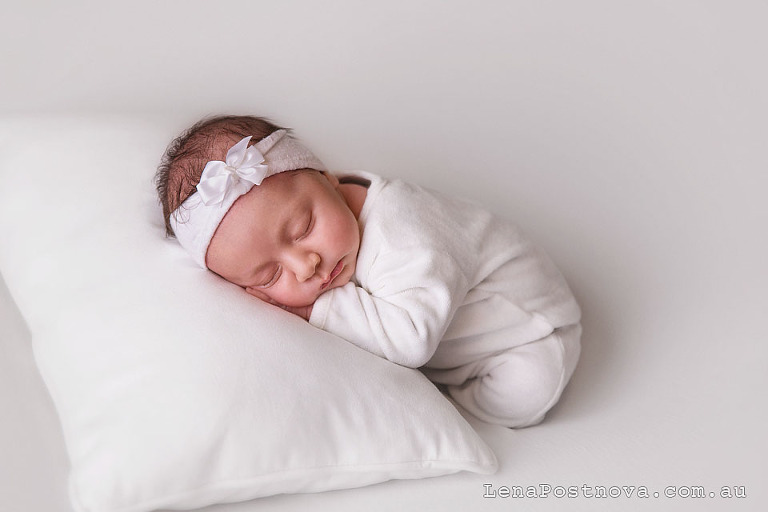 Natural style newborn photos of a baby girl wearing white sleeping on the pillow