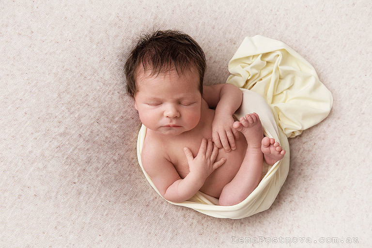 Newborn long haired baby girl sleeping on her back wrapped in the cream wrap