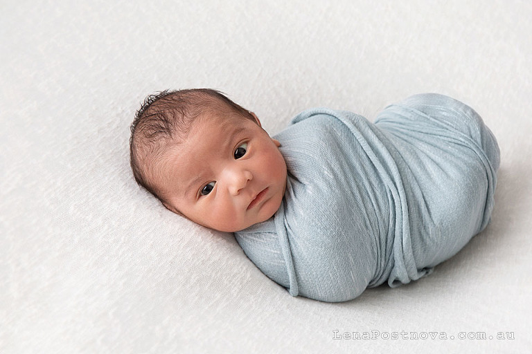 awake newborn baby boy wrapped in a blue swaddle