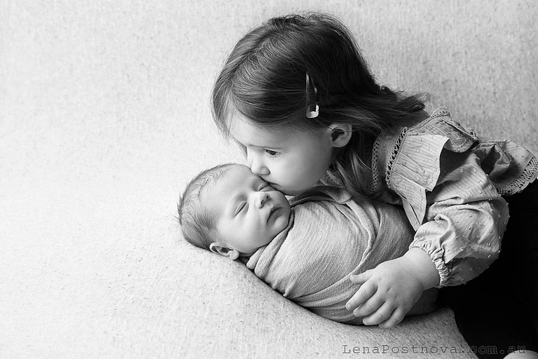 sister kissing her newborn brother ar Family newborn photoshoot